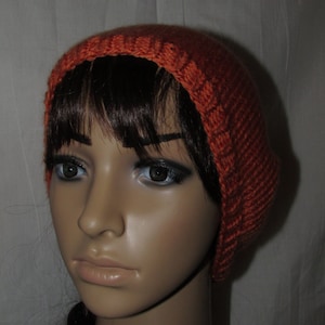 May include: A close-up of a person wearing a knitted orange beanie hat. The hat is made of a soft, warm material and has a simple design.