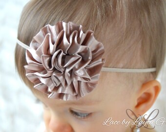 May include: A baby headband with a large, blush-colored satin flower. The headband is made of a thin, elastic material.
