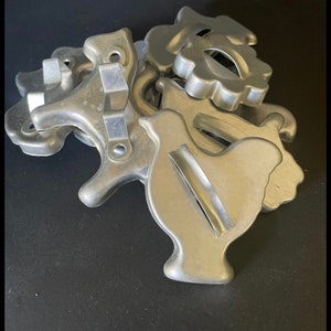 May include: A set of vintage metal cookie cutters in various shapes, including a chicken, a flower, and a heart. The cutters are made of silver-colored metal and have a worn, antique look.