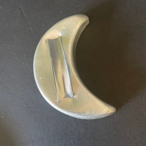 May include: A silver crescent moon cookie cutter. The cutter has a smooth, rounded edge and a flat, rectangular handle.