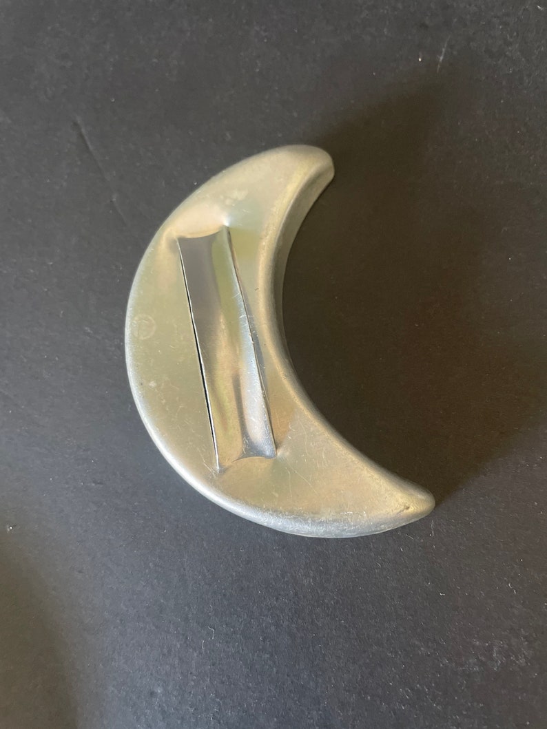 May include: A silver crescent moon cookie cutter. The cutter has a smooth, rounded edge and a flat, rectangular handle.