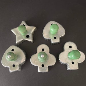 May include: Set of five vintage metal cookie cutters with wooden handles. The cutters are shaped like a star and four different playing card suits: hearts, clubs, and spades. The handles are green.