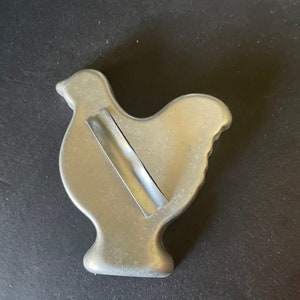 May include: A silver metal cookie cutter shaped like a chicken. The cutter has a small piece of tape on the back.