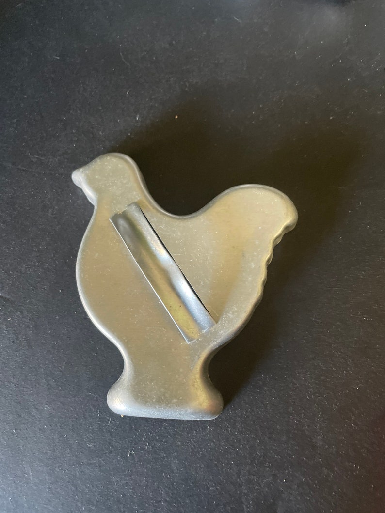 May include: A silver metal cookie cutter shaped like a chicken. The cutter has a small piece of tape on the back.