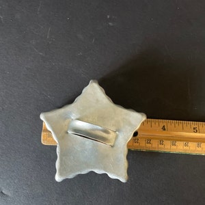May include: A silver metal star-shaped cookie cutter with a handle. The cutter is about 4 inches wide.