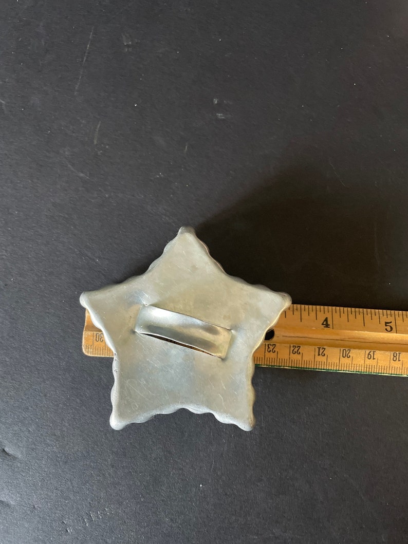 May include: A silver metal star-shaped cookie cutter with a handle. The cutter is about 4 inches wide.