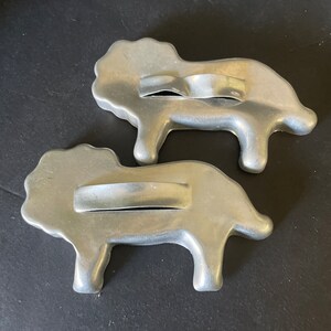 May include: Two vintage metal cookie cutters shaped like lions. The cutters are silver in color and have a handle on the top.
