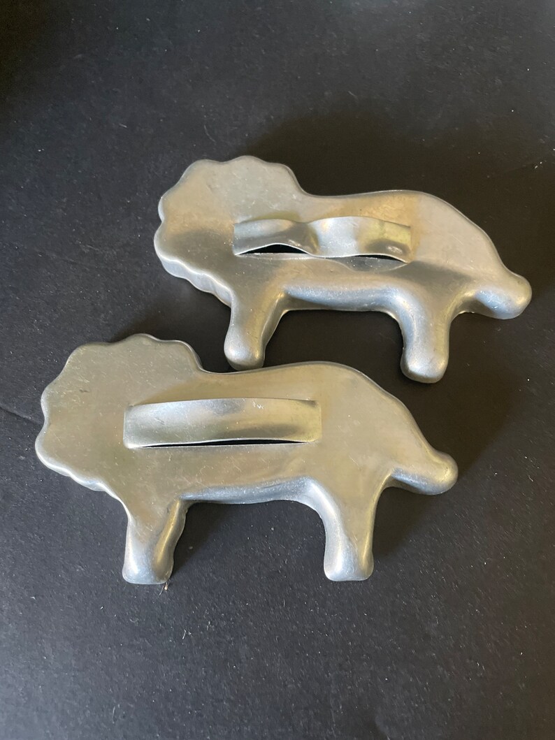 May include: Two vintage metal cookie cutters shaped like lions. The cutters are silver in color and have a handle on the top.
