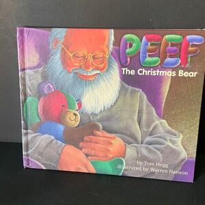 May include: A book cover with a colorful illustration of a bear named "Peef" on the front. The bear is wearing a red, green, and blue sweater and is being held by a man with a white beard. The title of the book is "Peef The Christmas Bear" and the author is Tom Hegg. The illustrator is Warren Hanson.