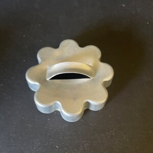 May include: A silver metal cookie cutter shaped like a flower with a small hole in the center.