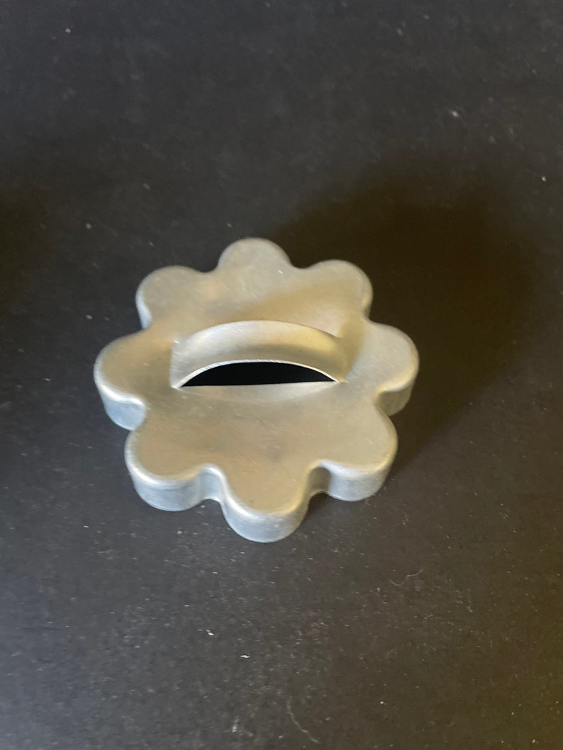 May include: A silver metal cookie cutter shaped like a flower with a small hole in the center.