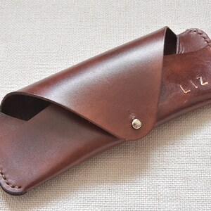 May include: A brown leather glasses case with the name "Liz" embossed on the front.