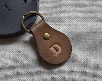Op de afbeelding: Een bruine leren sleutelhanger met een messing ring en een messing knoop. De sleutelhanger heeft de letter "D" erop gegraveerd.