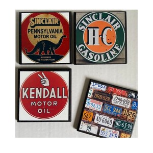May include: Four vintage-style square coasters with black frames. The top left coaster features a red, white, and black Sinclair Pennsylvania Motor Oil logo with a dinosaur illustration. The top right coaster features a green, orange, and white Sinclair HC Gasoline logo. The bottom left coaster features a red, white, and black Kendall Motor Oil logo with a hand making a peace sign. The bottom right coaster features a collage of vintage licence plates with various colours and numbers.