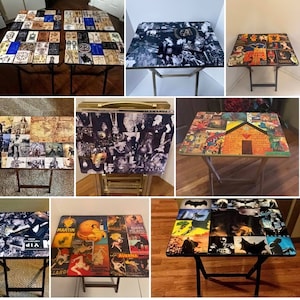 May include: A collection of ten folding tables with various colorful and patterned tabletops. The tabletops feature a variety of images, including vintage advertisements, maps, and comic book characters. The tables are all made of wood and have black metal legs.