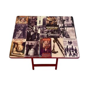 May include: A red folding table with a collage of vintage images featuring the magician Harry Houdini. The images include newspaper clippings, photographs, and posters. The table is made of wood and has a red finish.
