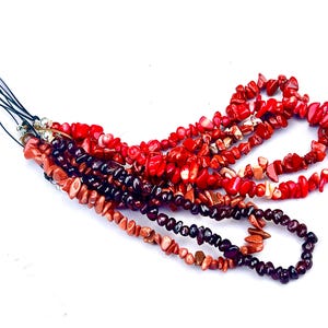 May include: A multi-strand beaded phone charm with red, brown, and black gemstone beads. The charm is attached to a black string.
