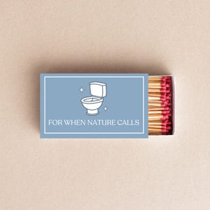 May include: A matchbox with a blue background featuring a white illustration of a toilet and the text "FOR WHEN NATURE CALLS." The match heads are red, and the box is open, revealing the matches.