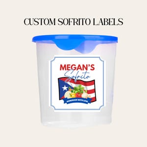 May include: A clear plastic container with a blue lid. The container has a label with the text "Megan's Sofrito" and a Puerto Rican flag design. The label also includes the text "Homemade with Love". The text "Custom Sofrito Labels" is above the container.
