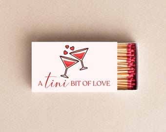 May include: A white matchbox with the text "A tini bit of love" and a graphic of two martini glasses with red liquid and hearts. The match heads are red.