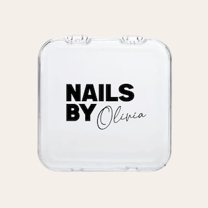 May include: A clear, square nail case with a hinged lid. The case features the text "NAILS BY Olivia" in black, bold font. The design is simple and modern, suitable for storing nail supplies.