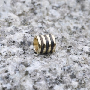 May include: A gold and black metal bead with a cylindrical shape and multiple rings.