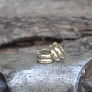 May include: Two gold-colored metal rings stacked on top of each other. The rings are smooth and have a rounded shape.