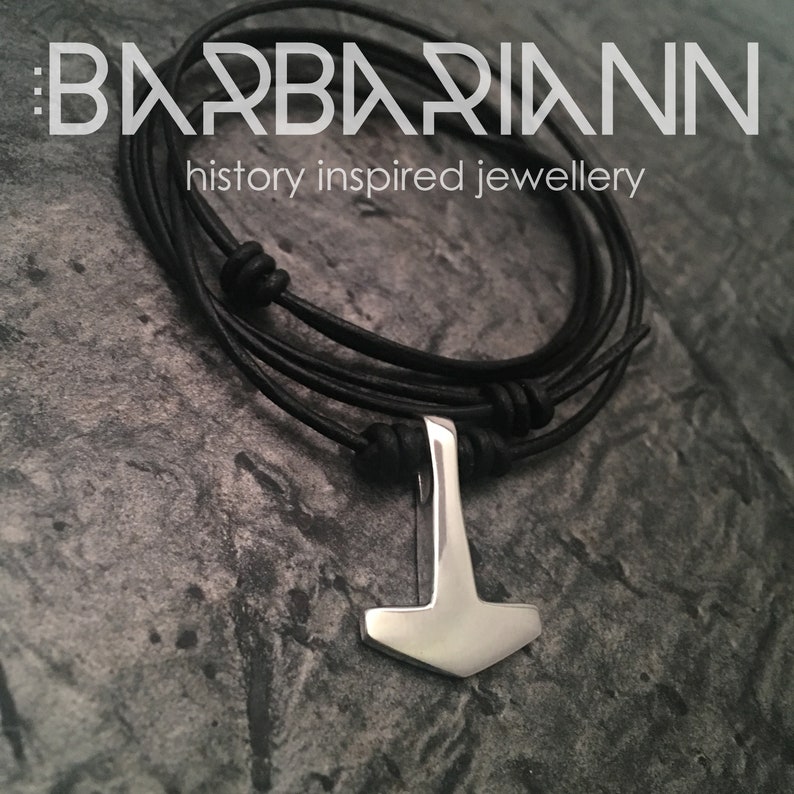 May include: A silver Mjolnir pendant on a black leather cord necklace. The necklace has a braided leather cord with knots and beads. The pendant is a replica of Thor's hammer.