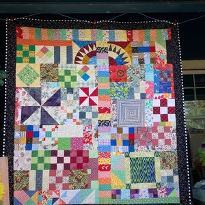 May include: A colorful patchwork quilt with a black and white border. The quilt is made up of many different squares and rectangles of fabric, each with a unique pattern. The quilt is hanging on a wall.