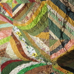 May include: A colorful quilt with a patchwork design featuring various shades of green, brown, yellow, and red. The quilt is made of different fabrics with floral and geometric patterns. The quilt is quilted with a swirling pattern.