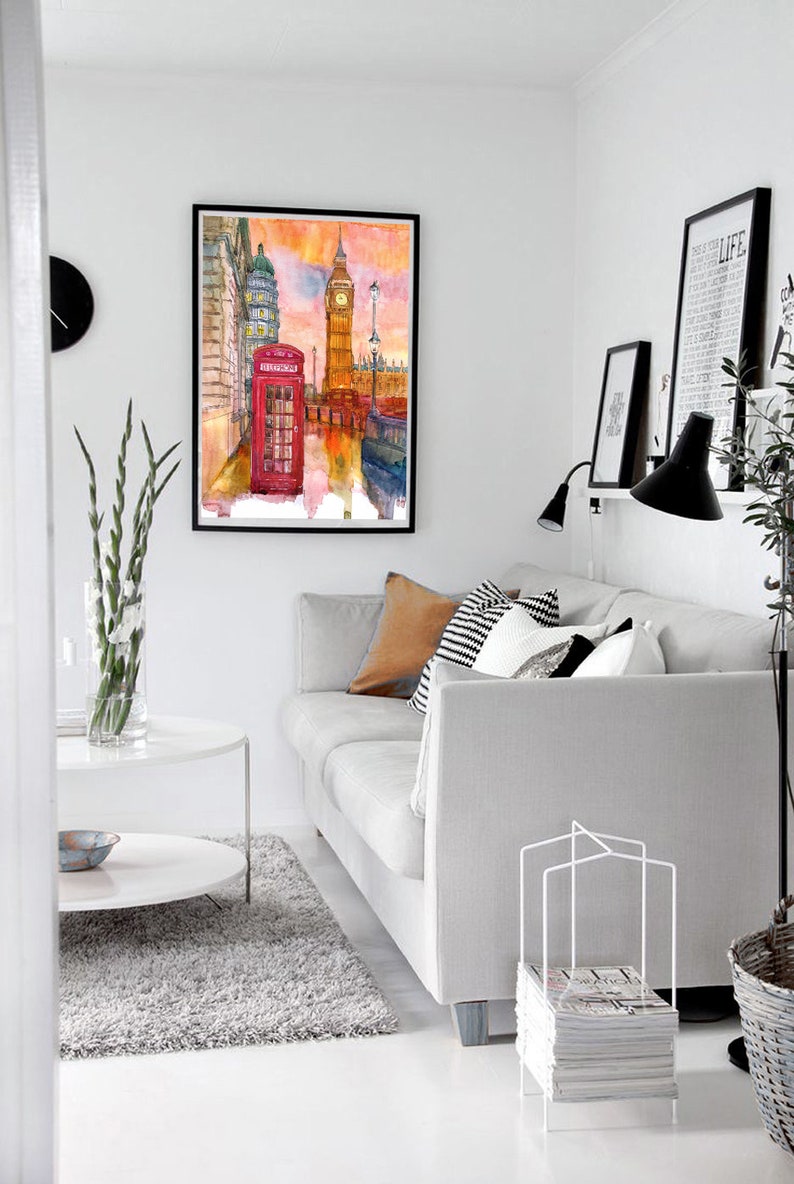 May include: A watercolor painting of Big Ben and a red telephone booth in London, England. The painting is framed and hanging on a white wall in a living room.