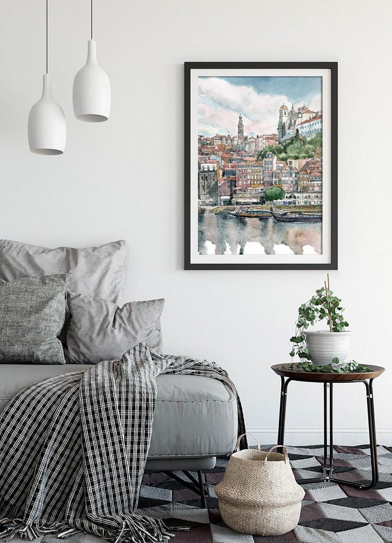 K&ouml;nnte beinhalten: Ein Aquarellbild einer Stadtlandschaft mit Geb&auml;uden, einem Fluss und Booten. Das Bild ist in einem schwarzen Rahmen gerahmt und h&auml;ngt an einer wei&szlig;en Wand.