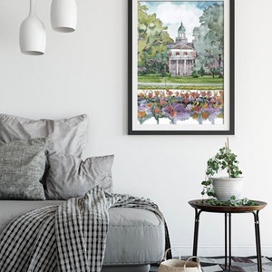 K&ouml;nnte beinhalten: Ein Aquarellbild eines Geb&auml;udes mit einer wei&szlig;en Fassade und einem gr&uuml;nen Dach. Das Geb&auml;ude ist von B&auml;umen und Blumen umgeben. Das Bild ist in Schwarz gerahmt und h&auml;ngt an einer wei&szlig;en Wand.