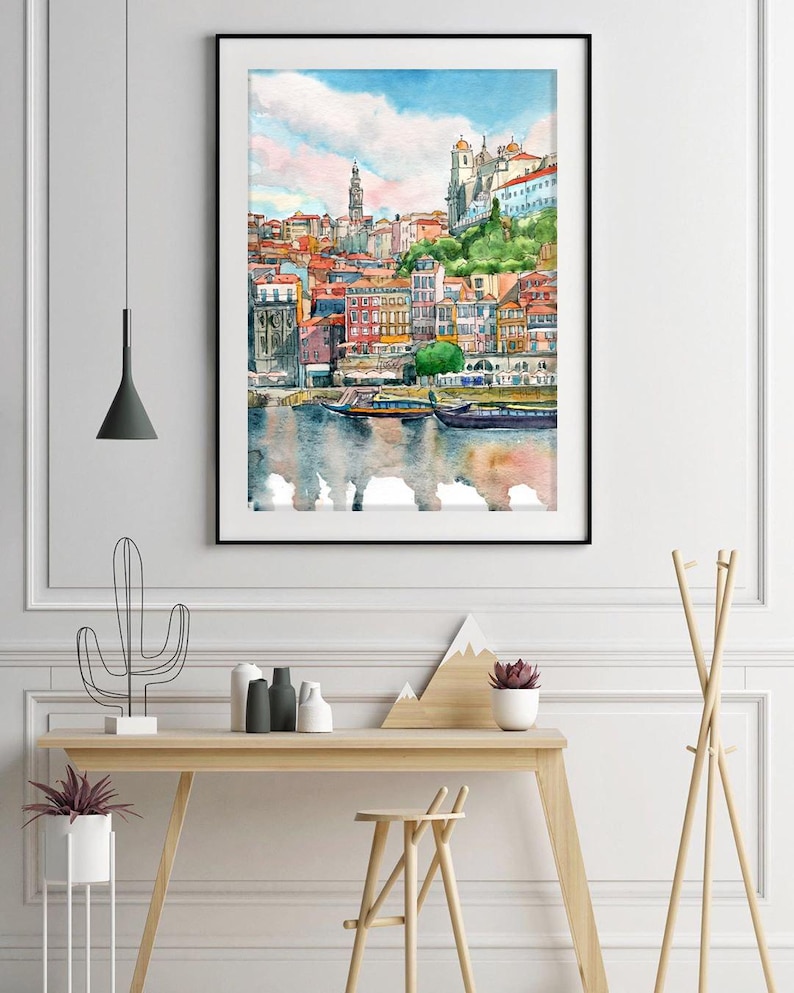 K&ouml;nnte beinhalten: Aquarellgem&auml;lde einer Stadtlandschaft mit bunten Geb&auml;uden und einem Fluss im Vordergrund. Die Geb&auml;ude sind dicht beieinander und haben verschiedene Architekturstile. Der Fluss ist ruhig und spiegelt den Himmel und die Geb&auml;ude wider.