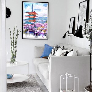 May include: A framed watercolor painting of a Japanese pagoda with cherry blossoms. The artwork features a red and blue pagoda, pink cherry blossoms, and a mountain in the background. The painting is displayed in a modern living room setting.