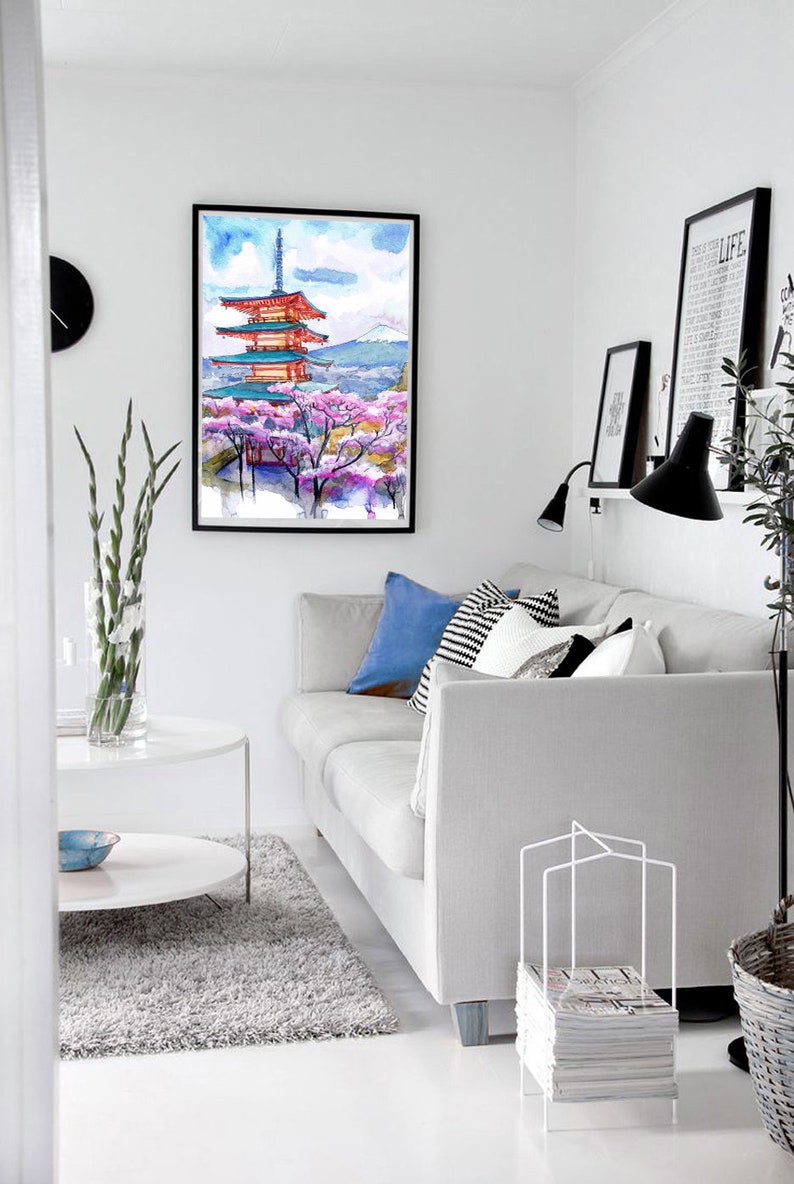 May include: A framed watercolor painting of a Japanese pagoda with cherry blossoms. The artwork features a red and blue pagoda, pink cherry blossoms, and a mountain in the background. The painting is displayed in a modern living room setting.