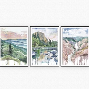 May include: Three watercolor paintings in black frames depicting different landscapes. The first painting shows a mountain range with a pink and orange sky. The second painting shows a river with rocks and a mountain in the background. The third painting shows a waterfall cascading down a rocky cliff.