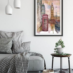 May include: A watercolor painting of a red telephone booth in front of Big Ben and other buildings in London, England. The painting has a soft, dreamy feel with a pink and orange sky.