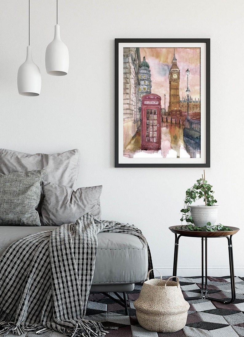 May include: A watercolor painting of a red telephone booth in front of Big Ben and other buildings in London, England. The painting has a soft, dreamy feel with a pink and orange sky.