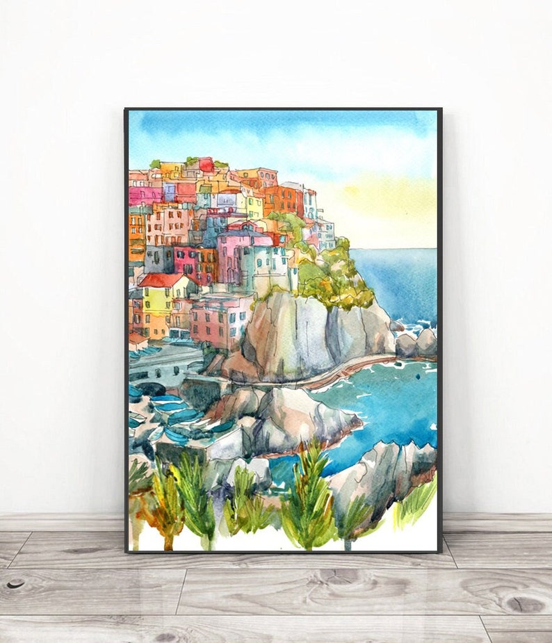 K&ouml;nnte beinhalten: Aquarellmalerei eines italienischen K&uuml;stendorfes. Das Kunstwerk zeigt farbenfrohe Geb&auml;ude auf einer Klippe mit Blick auf das Meer. Der Himmel ist blau mit einem gelben Farbverlauf und das Wasser ist t&uuml;rkis.