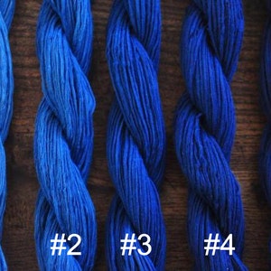 May include: Five skeins of blue yarn, numbered 1 through 5, are displayed on a wooden surface. The yarn is arranged in a vertical line, with the darkest blue yarn at the bottom and the lightest blue yarn at the top.