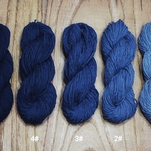 May include: Five skeins of yarn in varying shades of blue, from deep navy to light sky blue, are arranged in a row. Each skein is labeled with a number from 1 to 5, indicating a color variation. The yarn is displayed on a wooden surface.