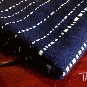 Puede incluir: Un trozo de tela azul oscuro doblado con un patrón geométrico blanco. La tela está doblada sobre sí misma y el patrón es visible en ambos lados.