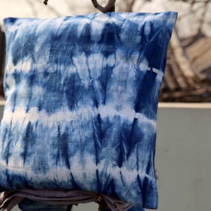 May include: A blue and white tie-dye pillow cover with a square shape. The pillow cover is made of a soft, textured fabric.