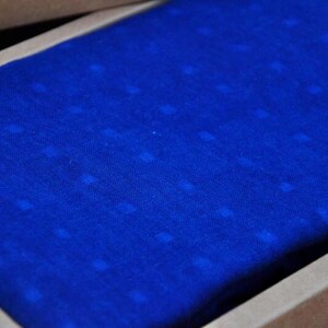 May include: A close-up of a blue fabric with a subtle white dot pattern. The fabric is folded and placed inside a brown box.