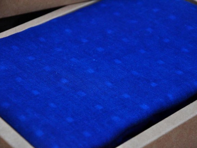 May include: A close-up of a blue fabric with a subtle white dot pattern. The fabric is folded and placed inside a brown box.