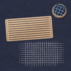 May include: A brown rectangular piece of cardboard with horizontal lines, a white grid pattern, and a blue and white pincushion with a geometric design.