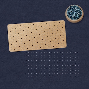 May include: A brown cork board with a grid of evenly spaced holes. The cork board is on a dark blue surface. A small, round, wooden pincushion with a blue and white geometric pattern is in the top right corner of the image.