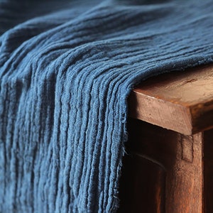 Può includere: Primo piano di un tessuto blu con superficie testurizzata. Il tessuto è drappeggiato su una superficie di legno.