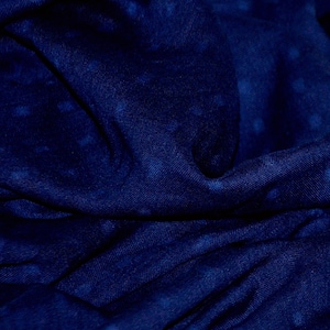May include: A close-up of a dark blue fabric with a subtle textured pattern. The fabric is folded and draped, creating soft folds and shadows.